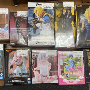 Assorted boxed anime action figures laid out on a table, featuring characters from Dragon Ball and other popular series (collectible figure boxes).