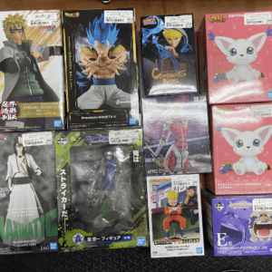 Assorted boxed anime action figures displayed on a wooden table, including Dragon Ball Z and Naruto characters along with pink cat boxes.