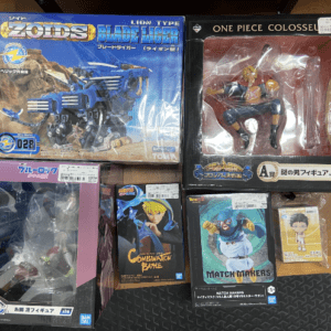 Collection of boxed action figures and model kits on a wooden floor, including Zoids Blade Liger and One Piece Colosseum figures.