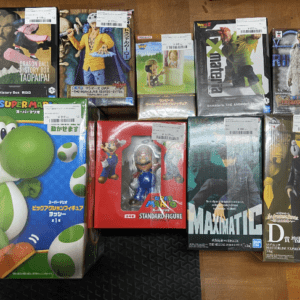 Boxed video game character figures arranged on a wooden floor, including Mario and Yoshi collectibles and other anime/figures boxed for display or sale.