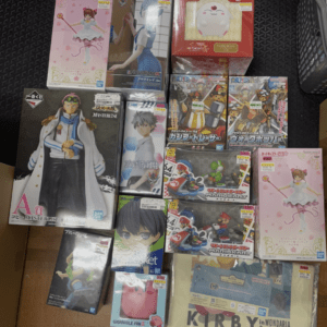 A top-down view of a collection of boxed anime figures and collectibles stacked on a black surface.