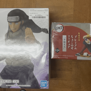 Two boxed anime figures on a wooden floor: a large Naruto figure on the left and a Demon Slayer figure on the right.