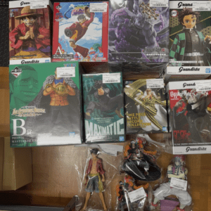 Shelf of anime figure boxes (One Piece, Dragon Ball, and Demon Slayer styles) arranged in two rows with loose figures on the bottom shelf, colorful character boxes facing forward for display.