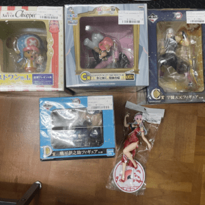 Group of boxed anime figures arranged on a wooden floor, including Chopper from One Piece in pink packaging and several other colorful character boxes.