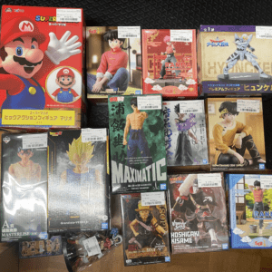 Boxed collection of Japanese anime and game figures laid on the floor, dominated by a large Mario box and various character figures by Bandai/Good Smile.
