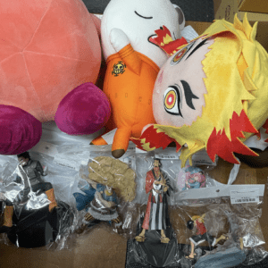 Assorted plush toys and small figurines arranged on a wooden table, including a peach-colored plush and a yellow-haired character.