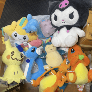 Pile of colorful plush stuffed animals on the floor, including a large black-and-white character with a pink skull on its head and several dragon-like toys.