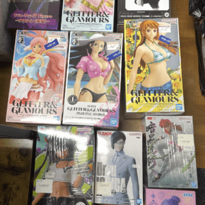 assortment of colorful anime figure boxes on a wooden floor, including Glitter & Glamours and One Piece figures