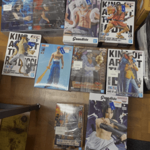 Assorted anime action figure boxes laid on a wooden floor, mostly Grandista figures with character boxes visible.