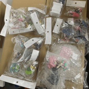 Assorted small vinyl figurines in clear bags with price tags, laid out on a brown table surface.