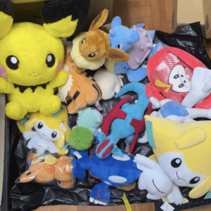 A pile of colorful stuffed animals and plush toys in a black container, including yellow, blue, green, and pink characters.