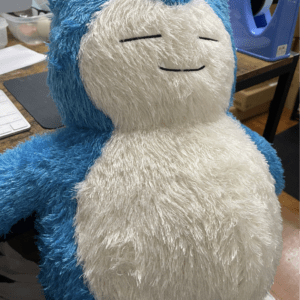 Blue and white fluffy plush toy with a calm, closed-eye expression, sitting on a desk.
