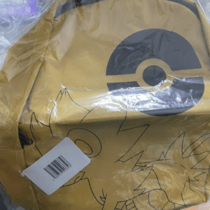 Yellow backpack in plastic wrap with a large gray circular logo and black doodle drawings, tag attached.