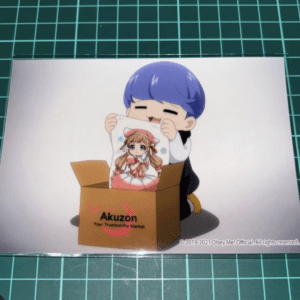 Chibi character with blue hair unboxes a print of a girl in a pink dress from an Akuzon box.