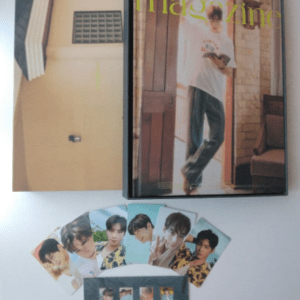 Framed magazine cover propped on a wall showing a man in a white shirt; below are fan photo cards of an idol group laid out on a white surface.
