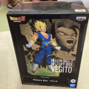 Dragon Ball Z History Box Vegito action figure in packaging, blue outfit and yellow hair, with background artwork on the box surface.