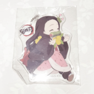Demon Slayer keychain in clear packaging showing a chibi-style girl with long black hair in a pink dress, hugging a green scarf.