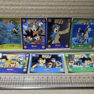 Eight Dragon Ball GT trading cards laid in two rows on a concrete surface, with a ruler at the bottom for scale.