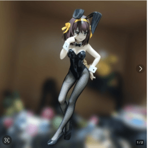 Anime-style bunny girl figurine in a black glossy leotard with fishnet stockings, bow tie, and yellow ribbon in hair, posed playfully.