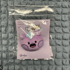 Purple round plush character with a smiling face in clear plastic packaging on a pastel card.