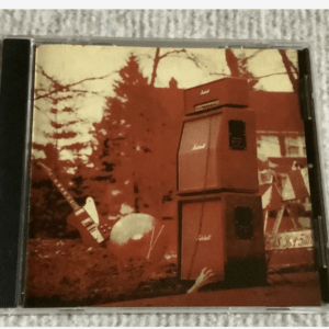 Red-tinted album cover showing a tall stack of Marshall guitar amplifiers beside a white electric guitar leaning on a rock in an outdoor scene with trees in the background.