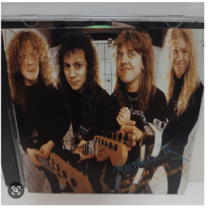 Four rock musicians with long hair pose with electric guitars in a tiled room; blue autograph across the photo.