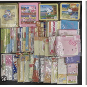 Colorful Hello Kitty stationery assortment: tin lunch boxes, notebooks, sticky notes, and folders spread on a dark surface.