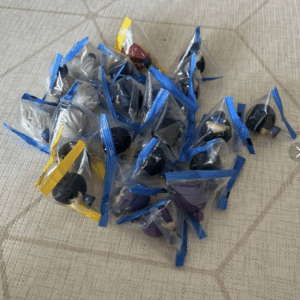 Assorted small toy figures sealed in clear bags with blue and yellow zip closures, laid on a light textured surface.