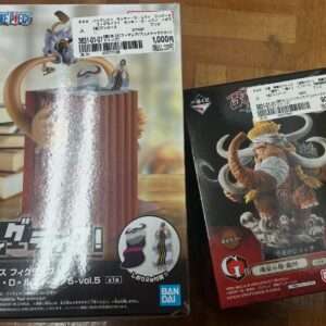 Two boxed One Piece figures: left box shows a character atop a tall wooden column with a price sticker, right box features a horned beast figure on rocks with Bandai logo.