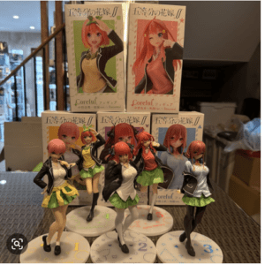 Display of anime figurine figures in school uniforms posed on circular bases, with boxed figures behind them on a table edge.