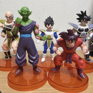 Five Dragon Ball Z action figures posed on orange bases, including Piccolo (green, purple outfit) and Goku (red outfit) in front. Behind them are to-be-identified characters in armor.