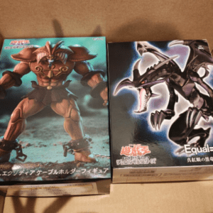 Two boxed action figures in a cardboard box: a muscular armored warrior/demon on the left and a black dragon figure on the right with Japanese text on the boxes