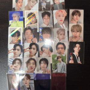 Collection of glossy photo cards featuring multiple K-pop group members arranged on a dark table, each card showing a different portrait.