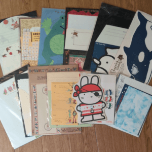 Assorted colorful notebooks and folders scattered on a wooden floor, featuring cartoon characters like Hello Kitty.