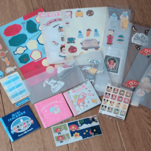 Assorted cute stickers and small stationery items spread on a wooden floor, including envelopes, stickers, and mini notepads.