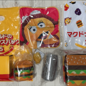 Assorted McDonald’s 2025 promotional tote bags and toys in yellow and white packaging, featuring a cartoon character and burger-themed items.