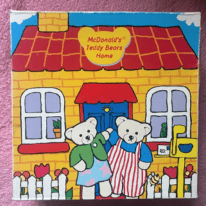 Colorful illustration of a yellow house labeled 'McDonald's Teddy Bears Home' with two teddy bears at the front.