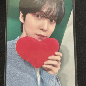 Young person with short dark hair holding a red plush heart near their face, wearing a light blue cardigan in a protective case.