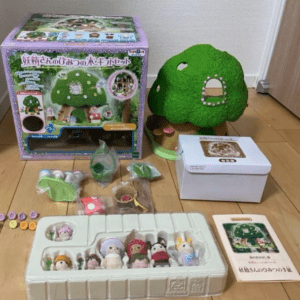 Green mossy tree-house toy with small figurines and accessories, boxed set on a wooden floor nearby the white storage box and instruction booklet.