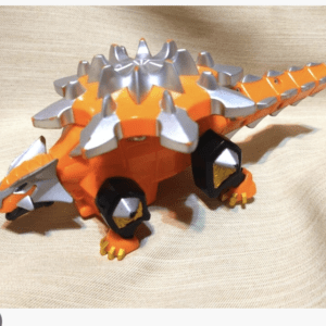 Orange toy dragon with silver spikes along its back, resting on beige fabric.