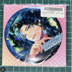 Round pin badge featuring a smiling anime character with teal hair, labeled 'Lucifer', on a pink polka-dot background with a barcode sticker in the corner.