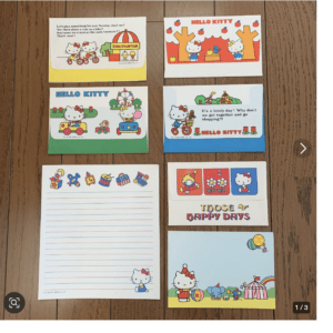Colorful Hello Kitty cards arranged on a wooden surface, featuring bright illustrations and captions on each card.