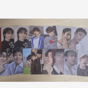 Photo cards featuring male K-pop idols lined up on a light wooden table, forming a fan collection.