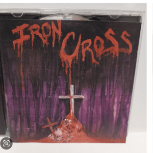 Album cover with red dripping 'IRON CROSS' text above a crucified cross on a mound of bones, set against a dark purple forest background.