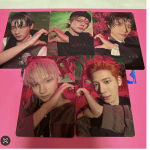 Six portrait photos of male K-pop idols arranged in a collage on a pink background, each making a heart with their hands.
