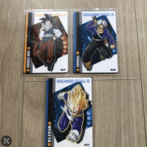 Three Dragon Ball Z trading cards on a beige surface: Goku (No.57), Trunks (No.58), and Vegeta in Super Saiyan form (No.61).