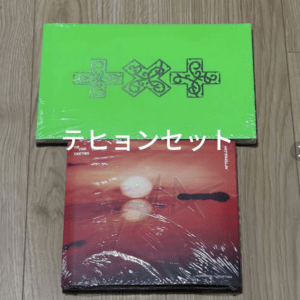 Two wrapped boxes on a wooden floor: a bright green ornate box on top of a red sunset album.