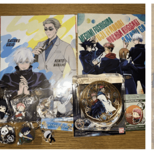 Collection of Jujutsu Kaisen merch on a wooden table: large posters of Satoru Gojo and Kento Nanami, plus a round decorative clock and keychains/charms.  Articulos Japan (Post Box Japan)
