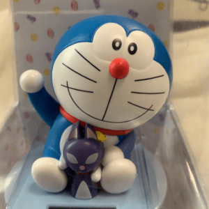 Blue Doraemon figure waving with a small purple cat toy sitting in its lap in a display case.