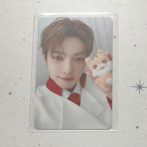 Young person in a white suit with red trim posing for a selfie, holding a small beige stuffed dog.